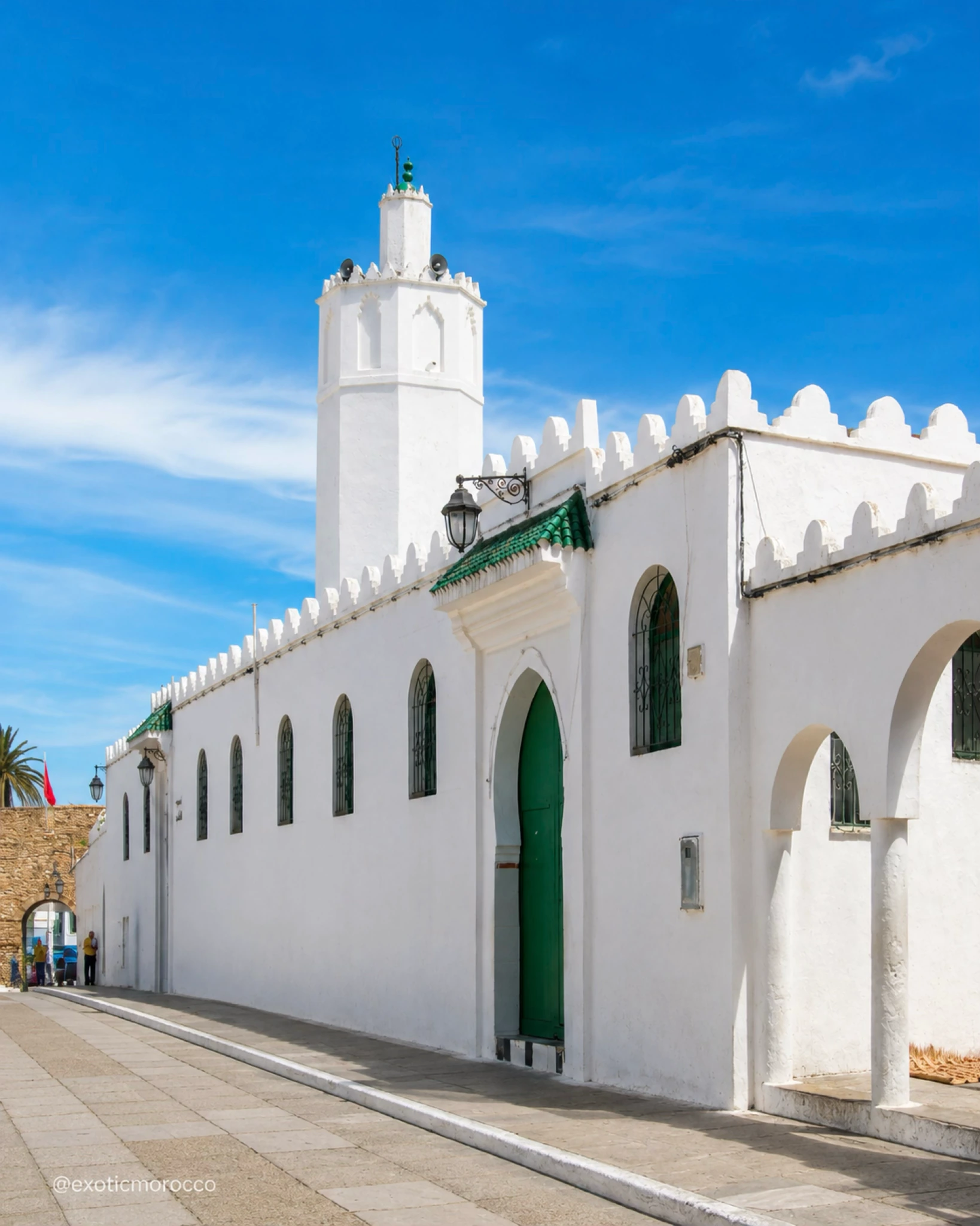 White mosque facade and minaret in Asilah with a green door under a blue sky