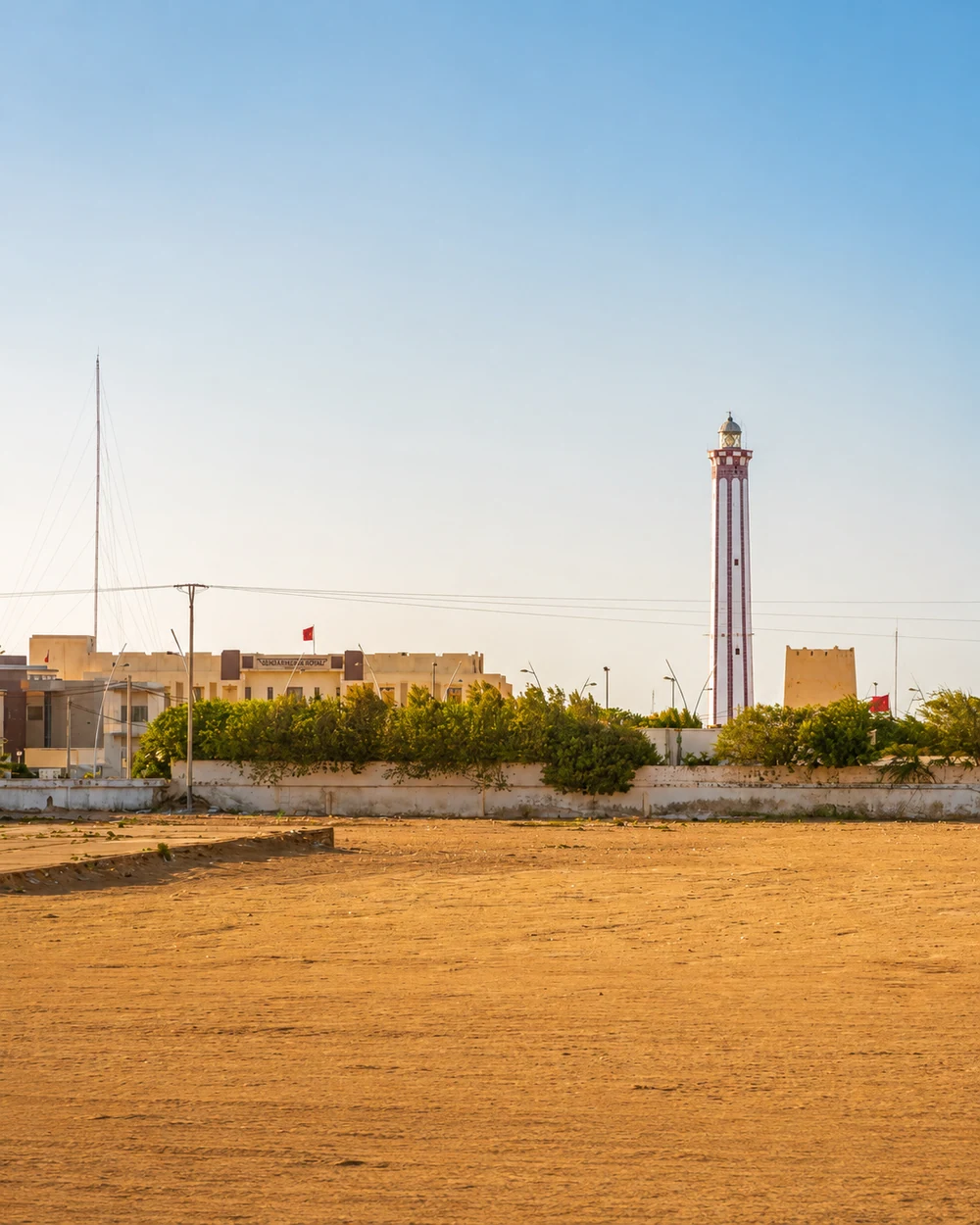 Boujdour lighthouse rising above low buildings and an open sandy foreground