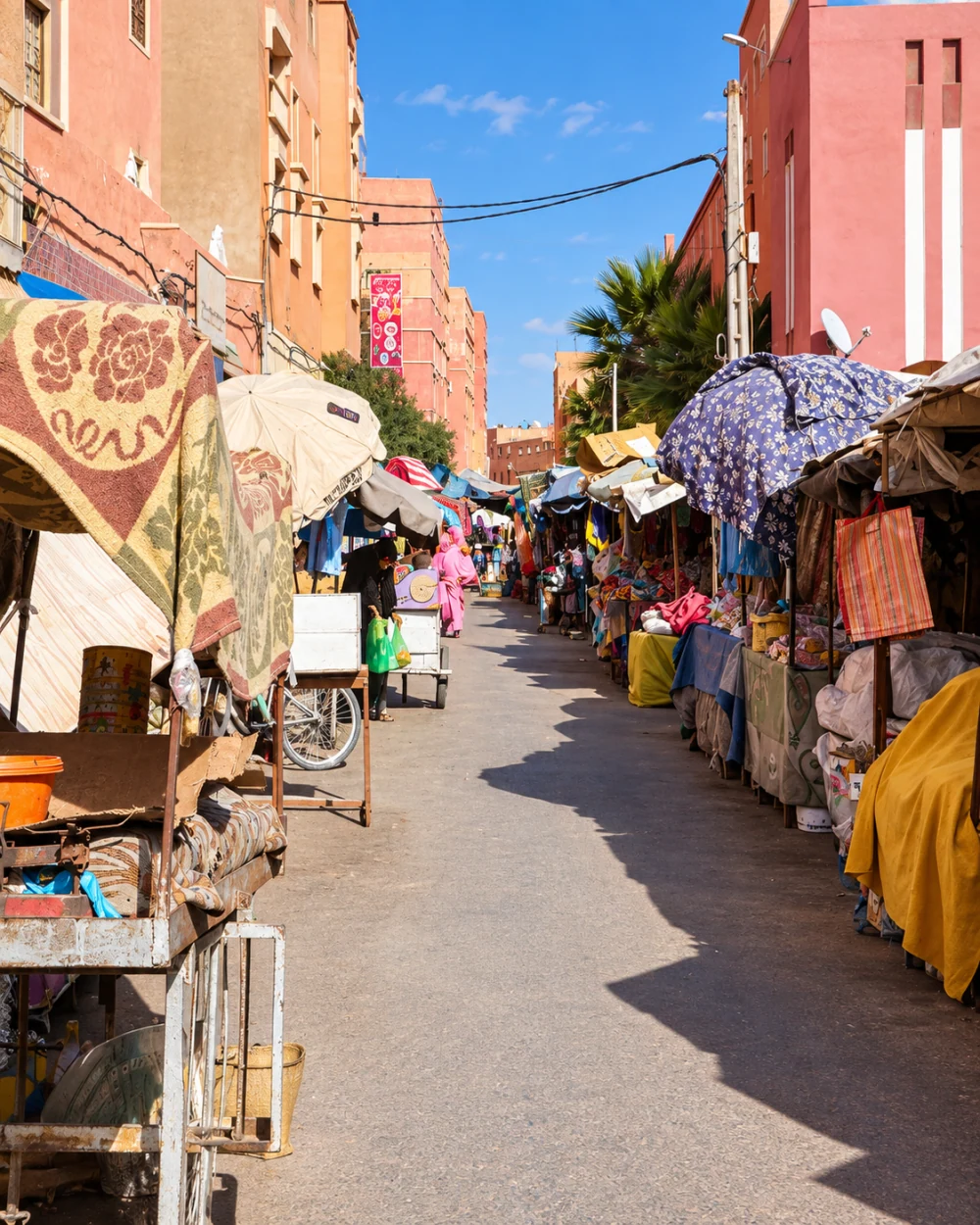 Textile stalls lining a narrow street between salmon-coloured buildings