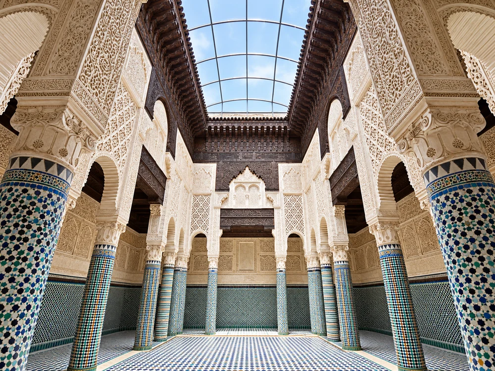 Carved stucco arches and zellige columns beneath the skylight of Salé’s Marinid Madrasa