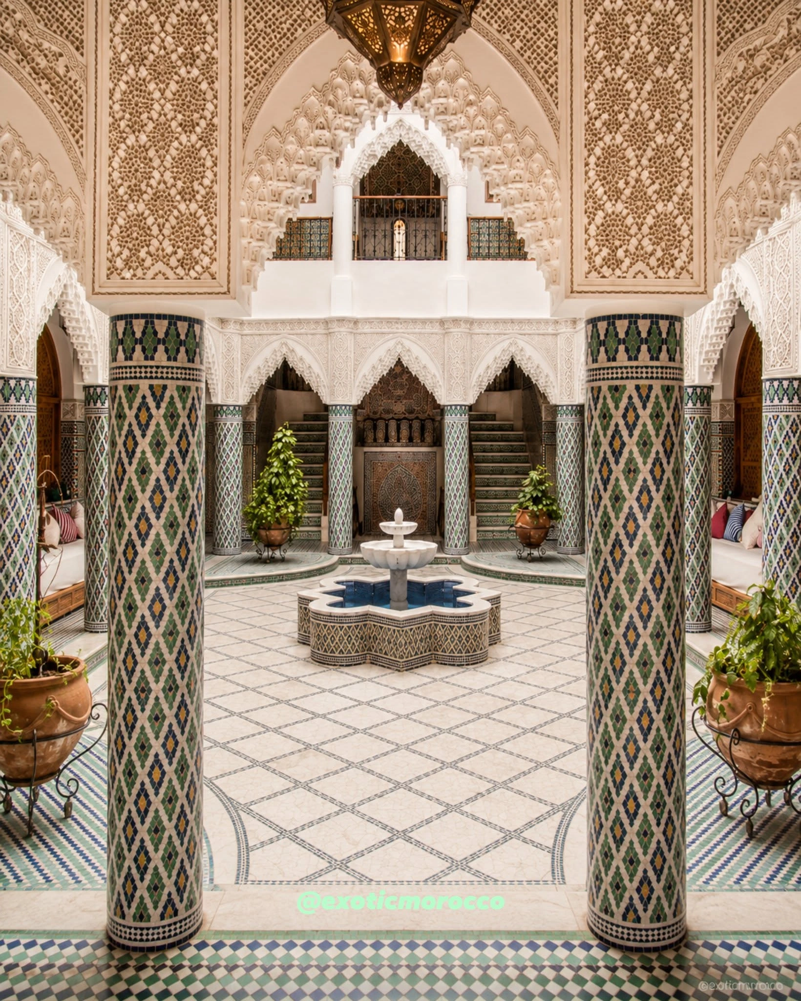 Moroccan riad courtyard with zellige columns, fountain and carved stucco details