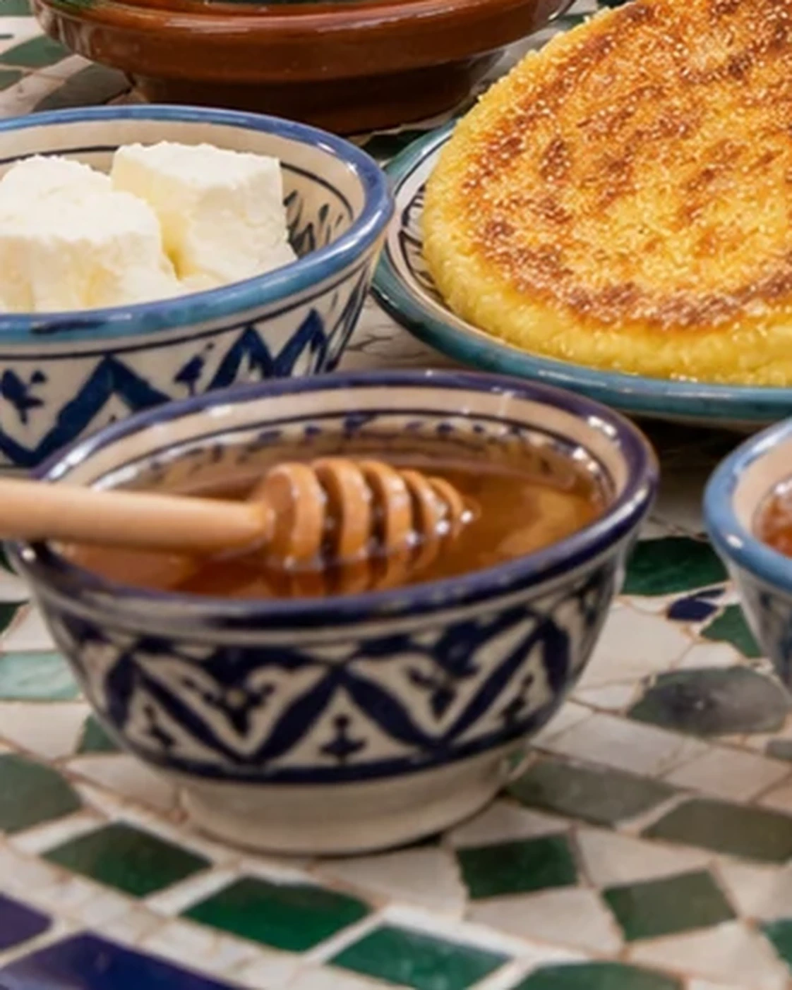 Honey in a patterned ceramic bowl with a wooden dipper
