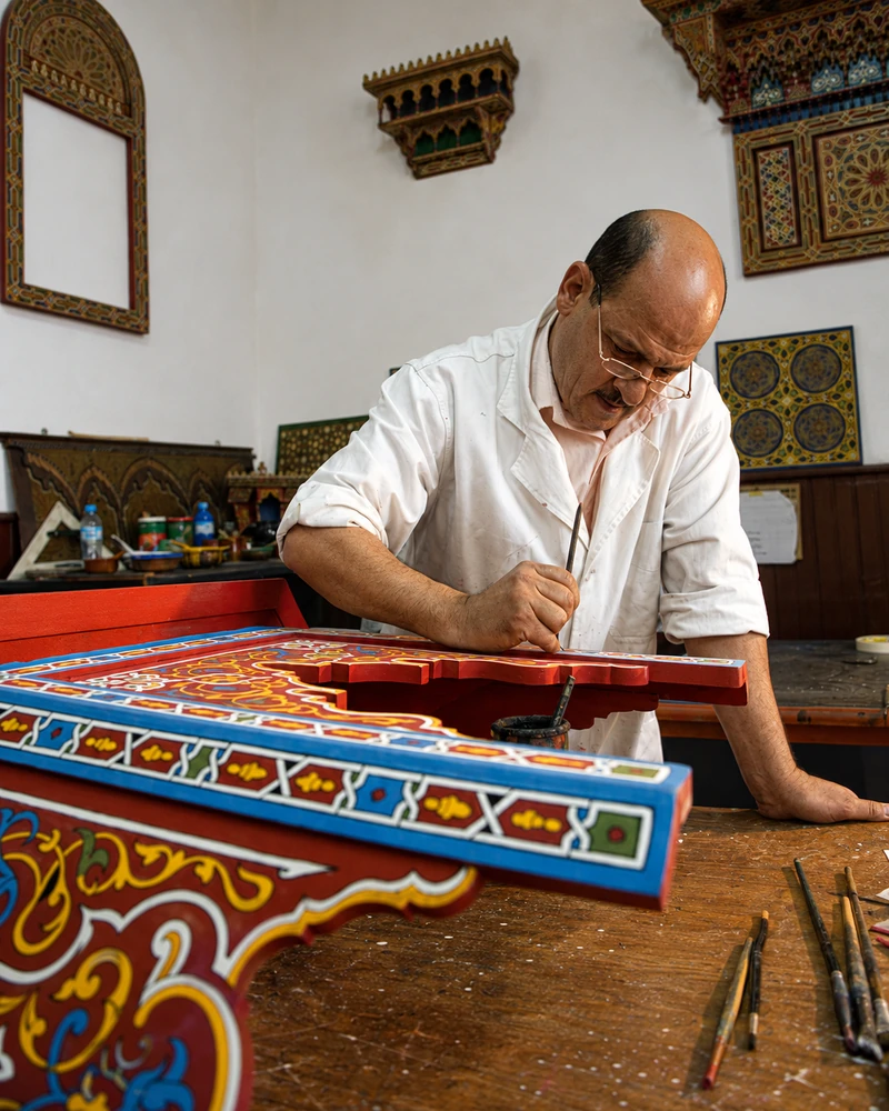 A craftsman painting a patterned wooden panel.