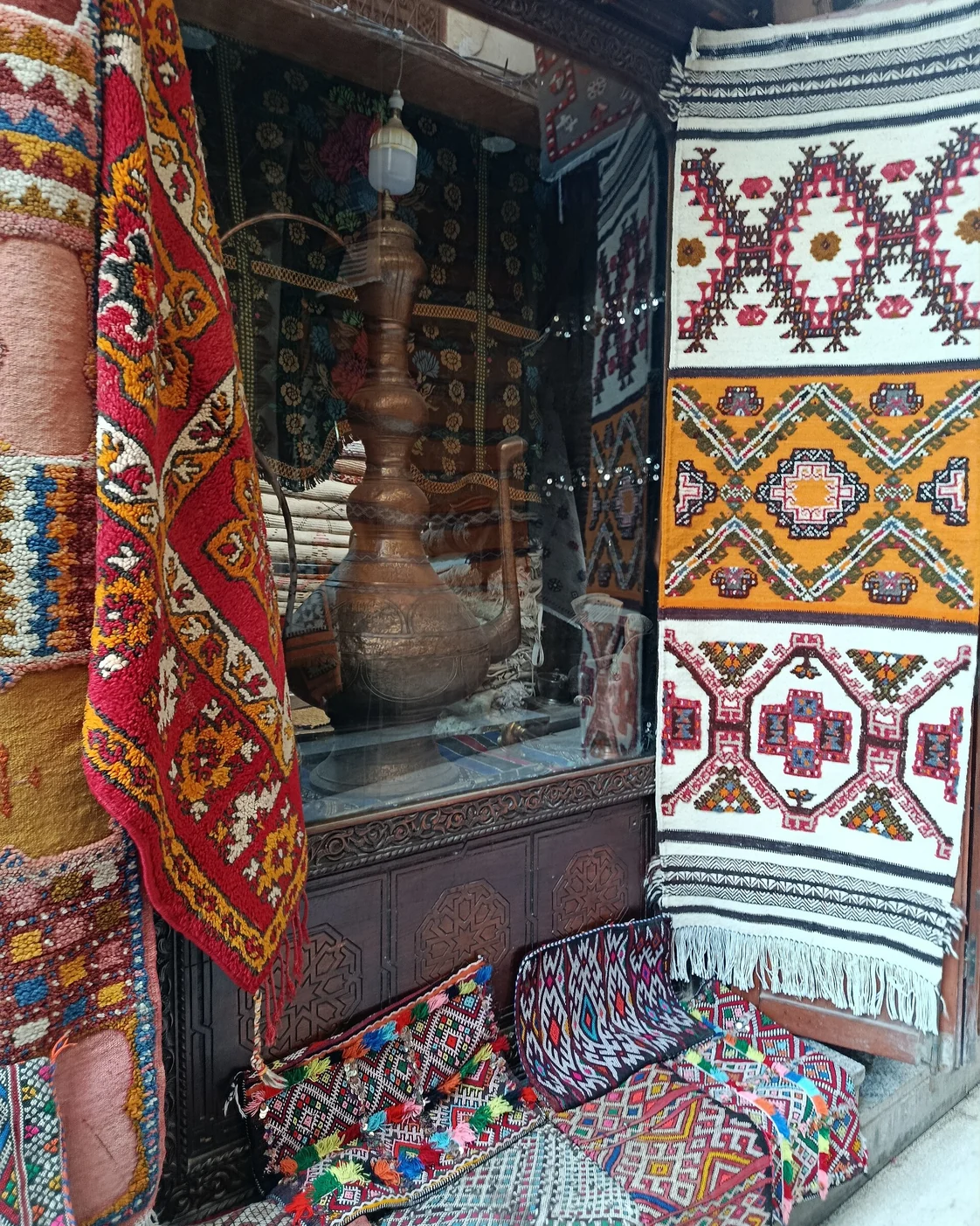 A large copper vessel and textiles displayed in a Fez shop.