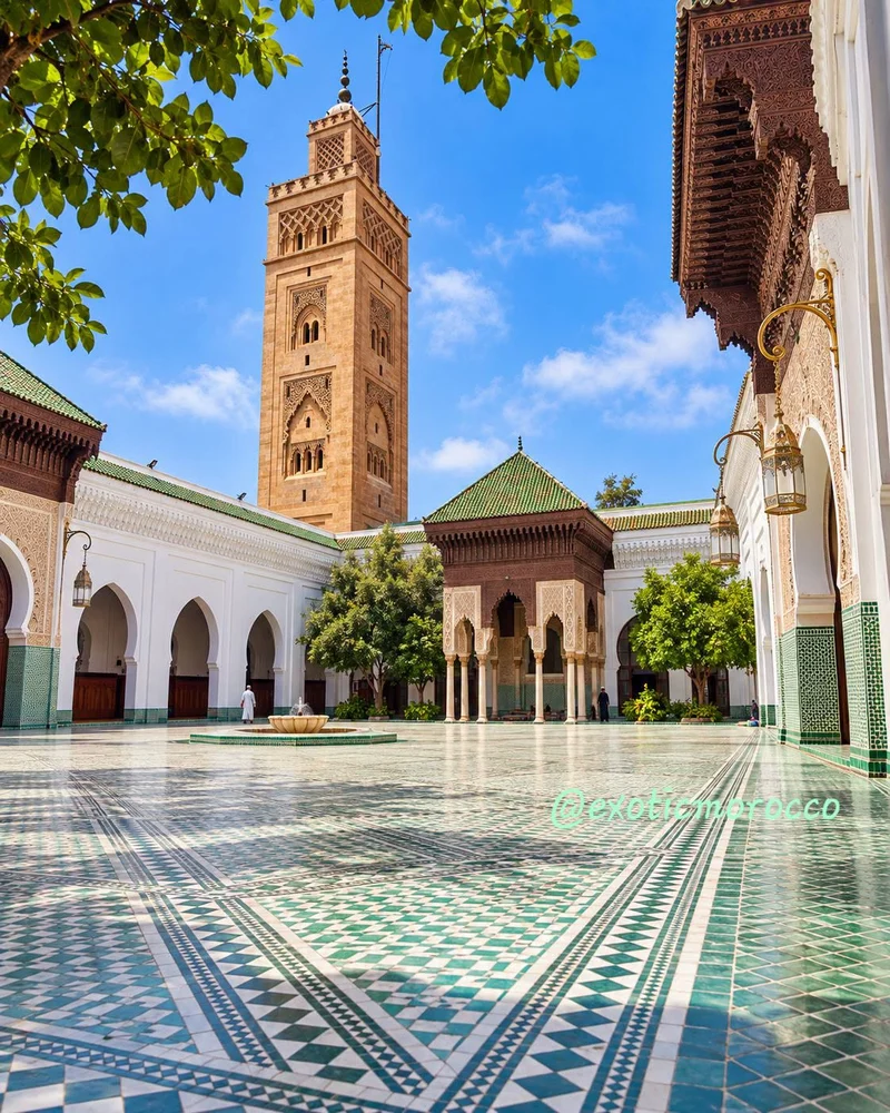 A Moroccan mosque courtyard with green and white zellige, a fountain, carved woodwork and a square minaret. Image supplied by Exotic Morocco.