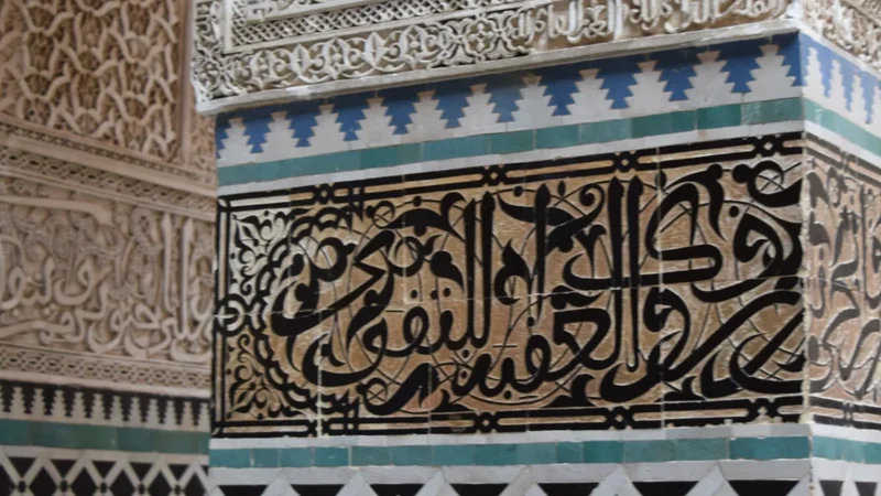 Detail of glazed geometric tilework, calligraphic borders and carved plaster around an opening.