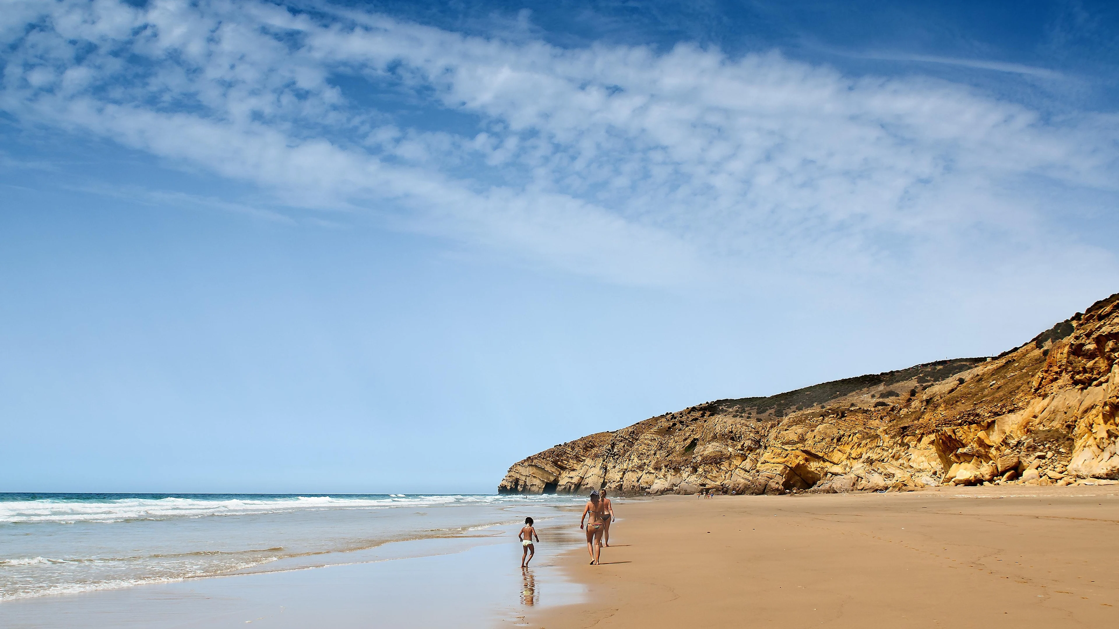 A broad sandy beach near Asilah with people walking by the water