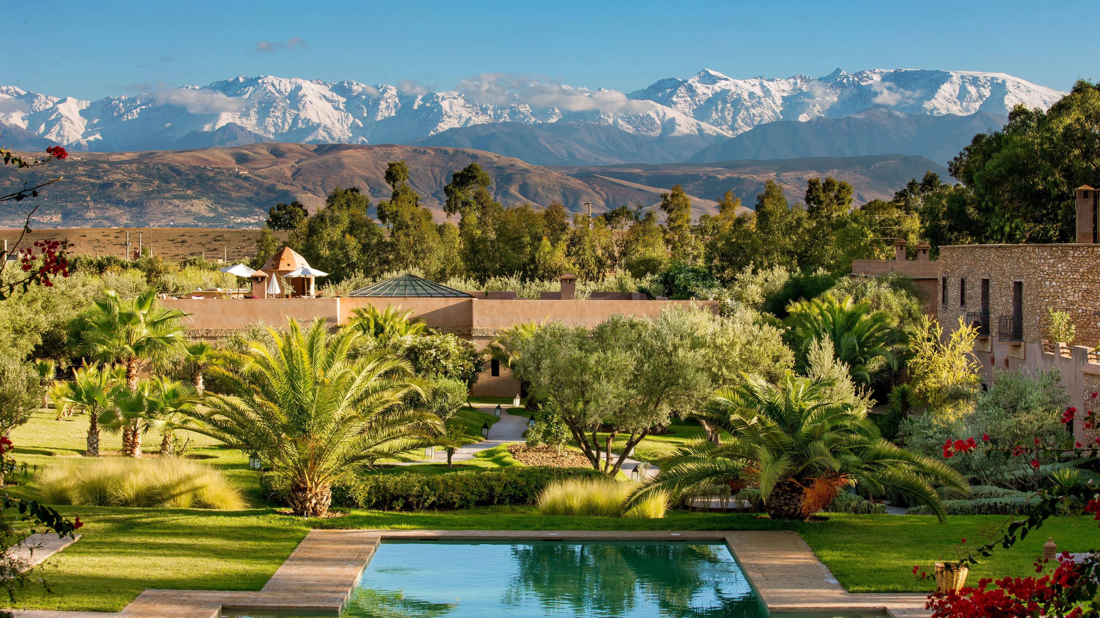 A garden and reflecting pool beneath snow-covered Atlas peaks