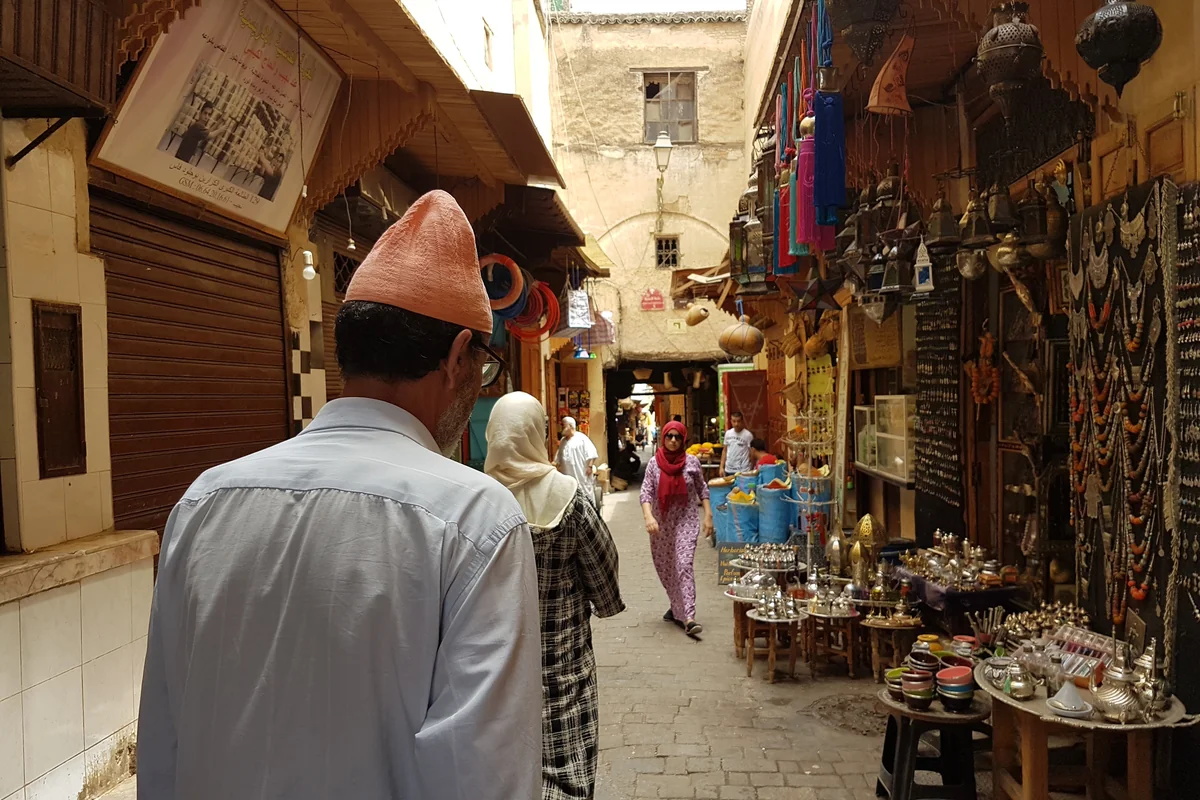 A person in a traditional cap walking along a Fès market lane