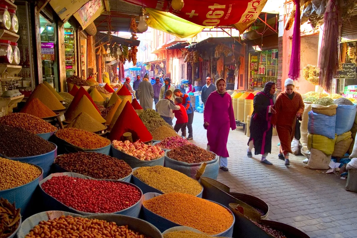 Spice stalls and shoppers along a Marrakech market lane