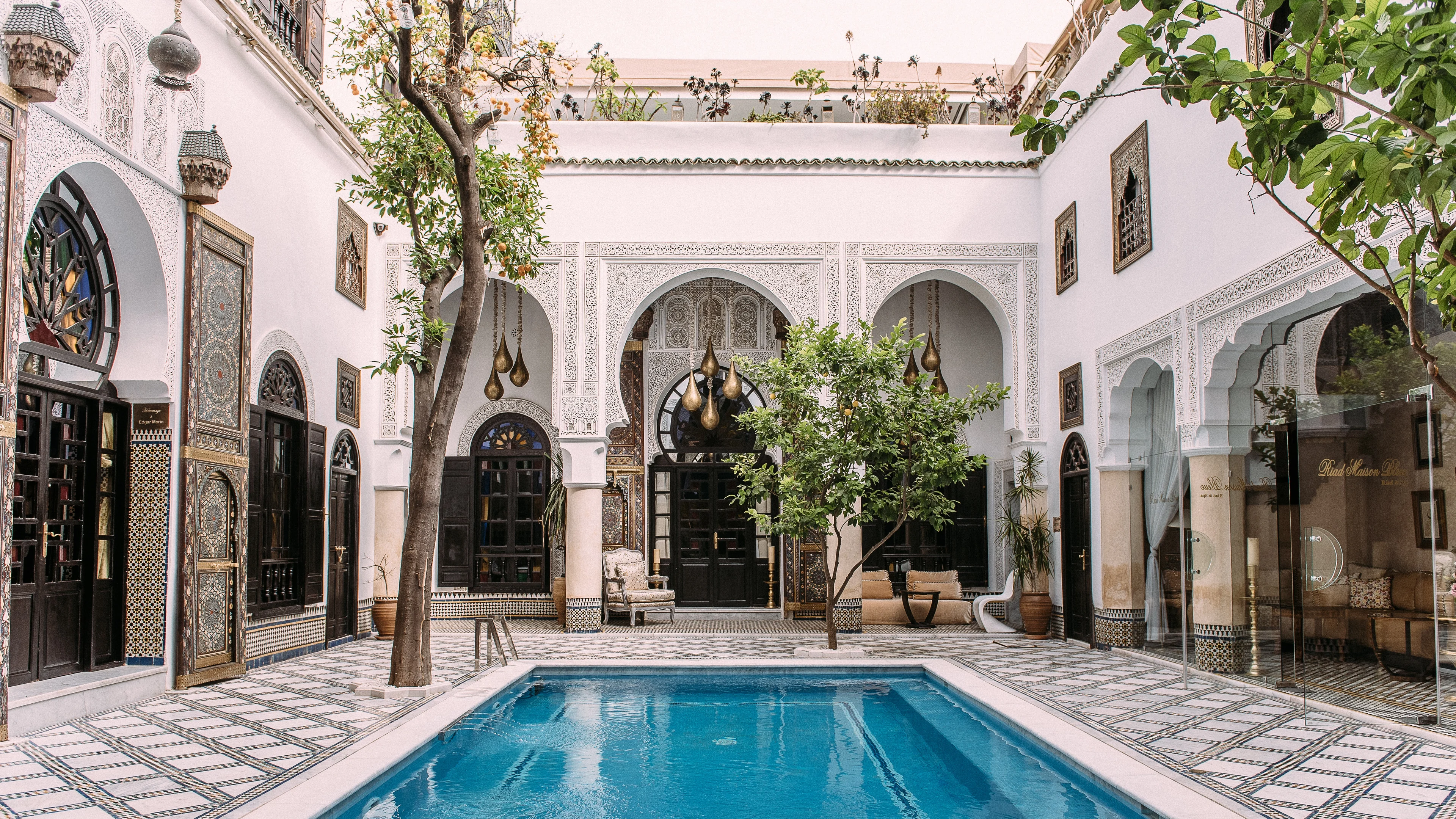 A traditional courtyard with a blue pool, tiled floor and white arches in Fès