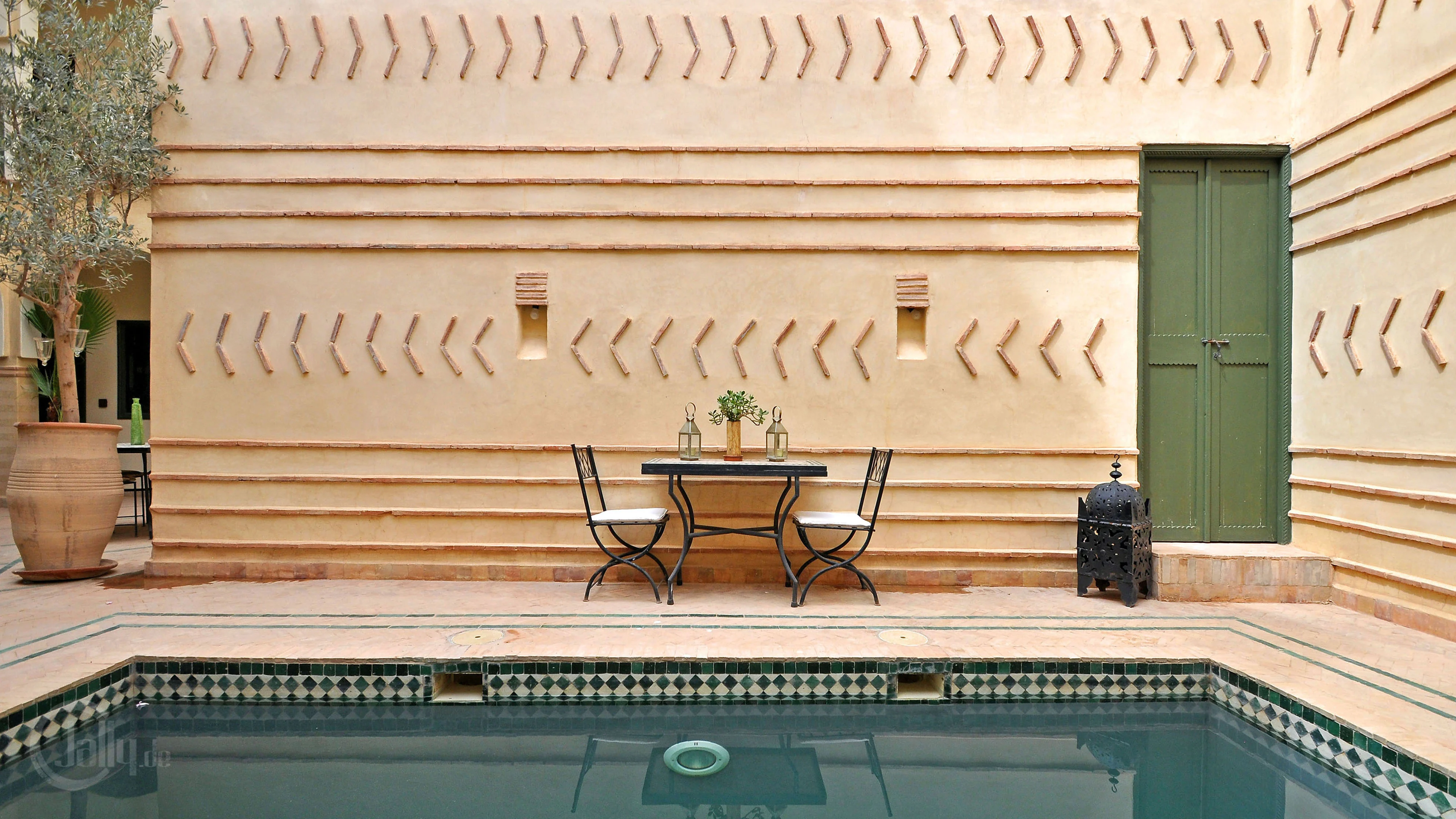 A calm Moroccan courtyard with a tiled pool, pale plaster and a green door