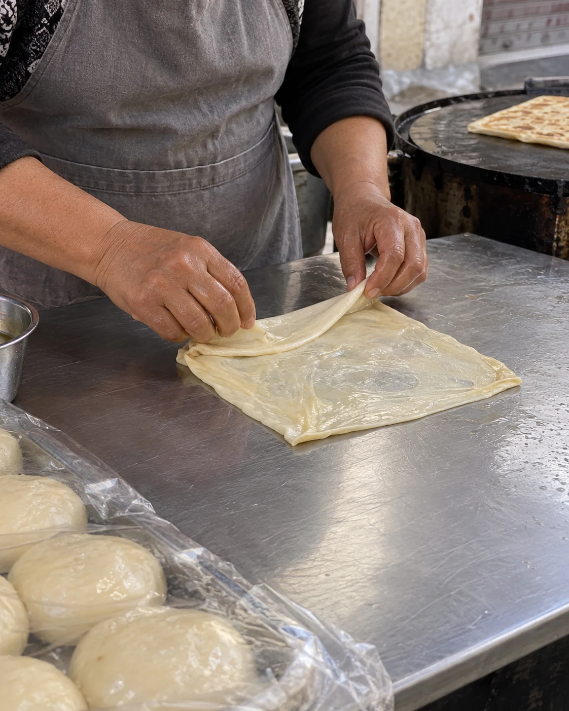 Hands folding thin dough at a food counter