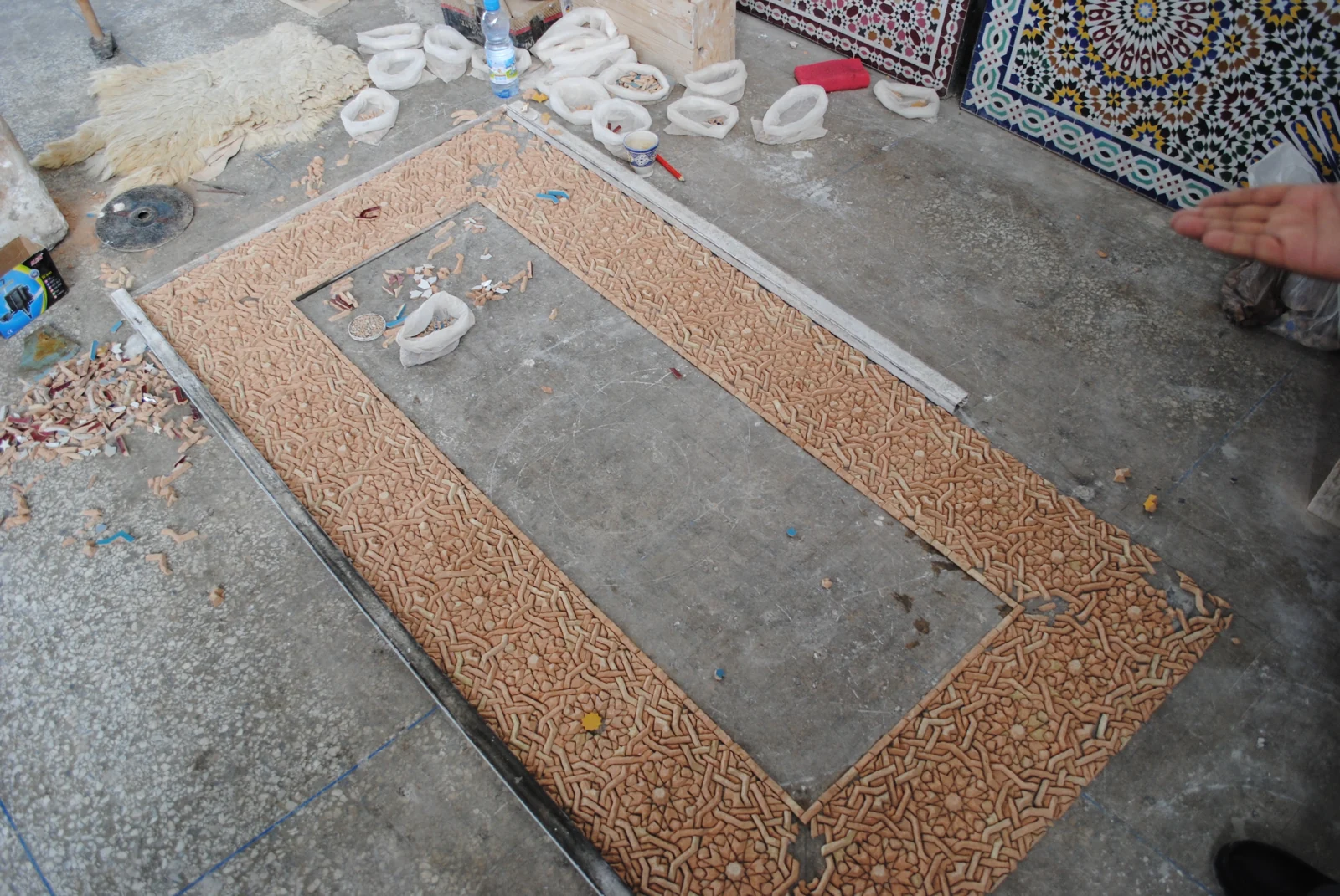 Mosaic pieces laid face down on a workshop floor, showing the terracotta backs of a border.