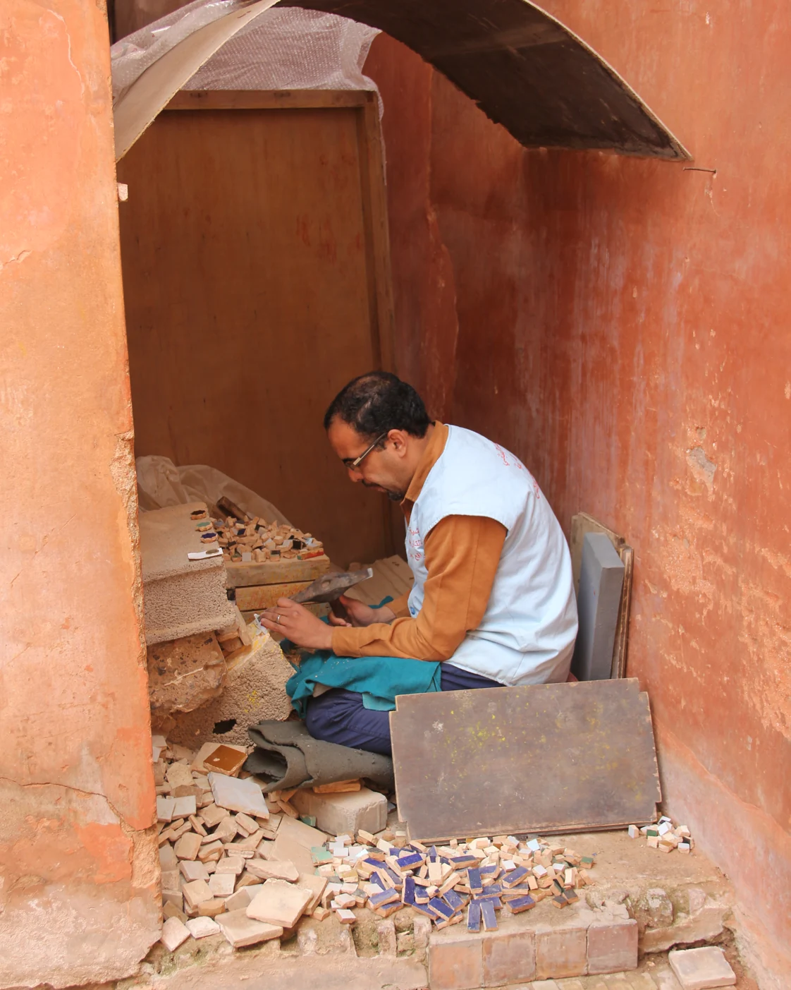 An artisan cuts mosaic pieces in an ochre-walled work area at the Saadian Tombs in Marrakech.