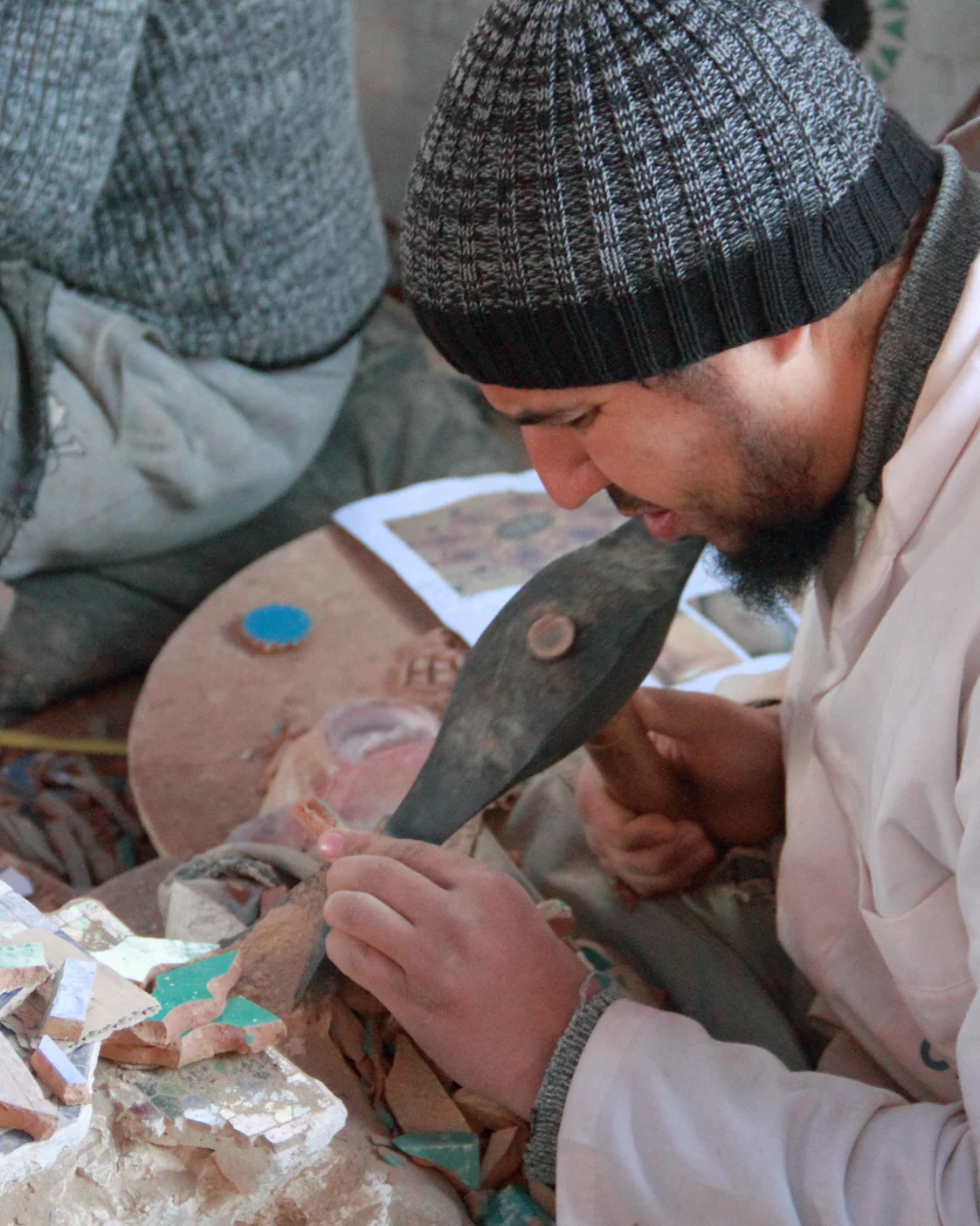 A zellige artisan in Fès cuts a small ceramic piece with a sharpened hammer.