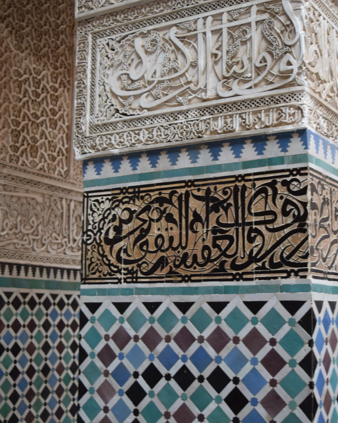 A corner at Al-Attarine where blue and green tile geometry meets an inscribed band and carved plaster.