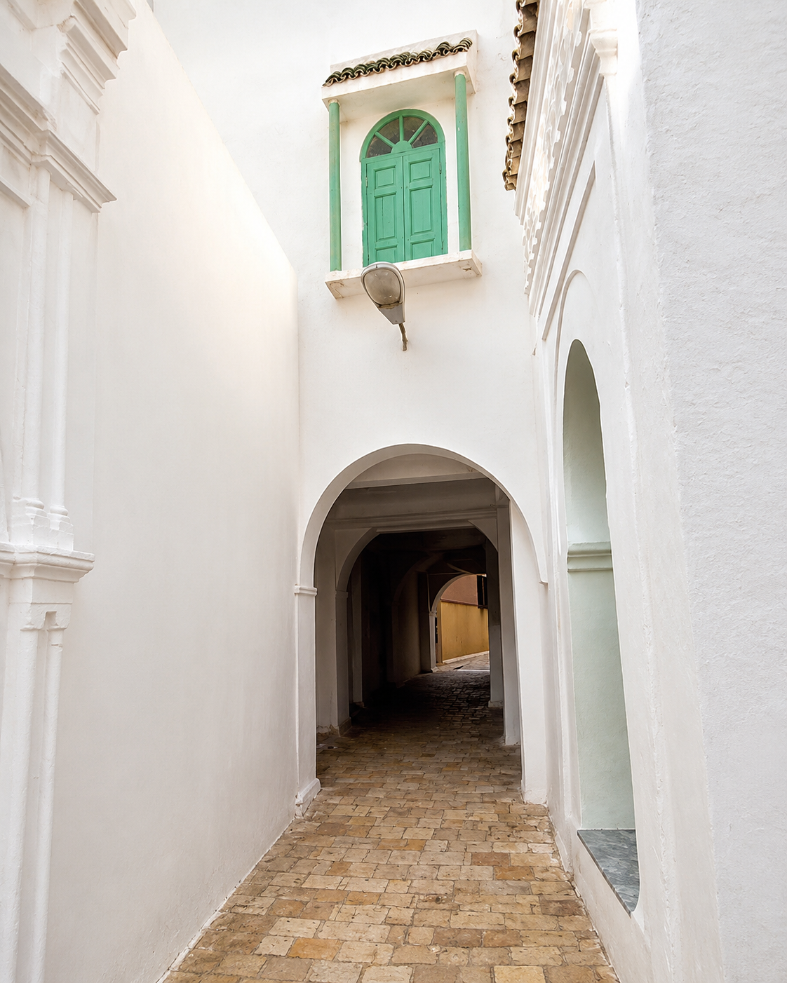 White arcaded lane with a green window and cobbled ground