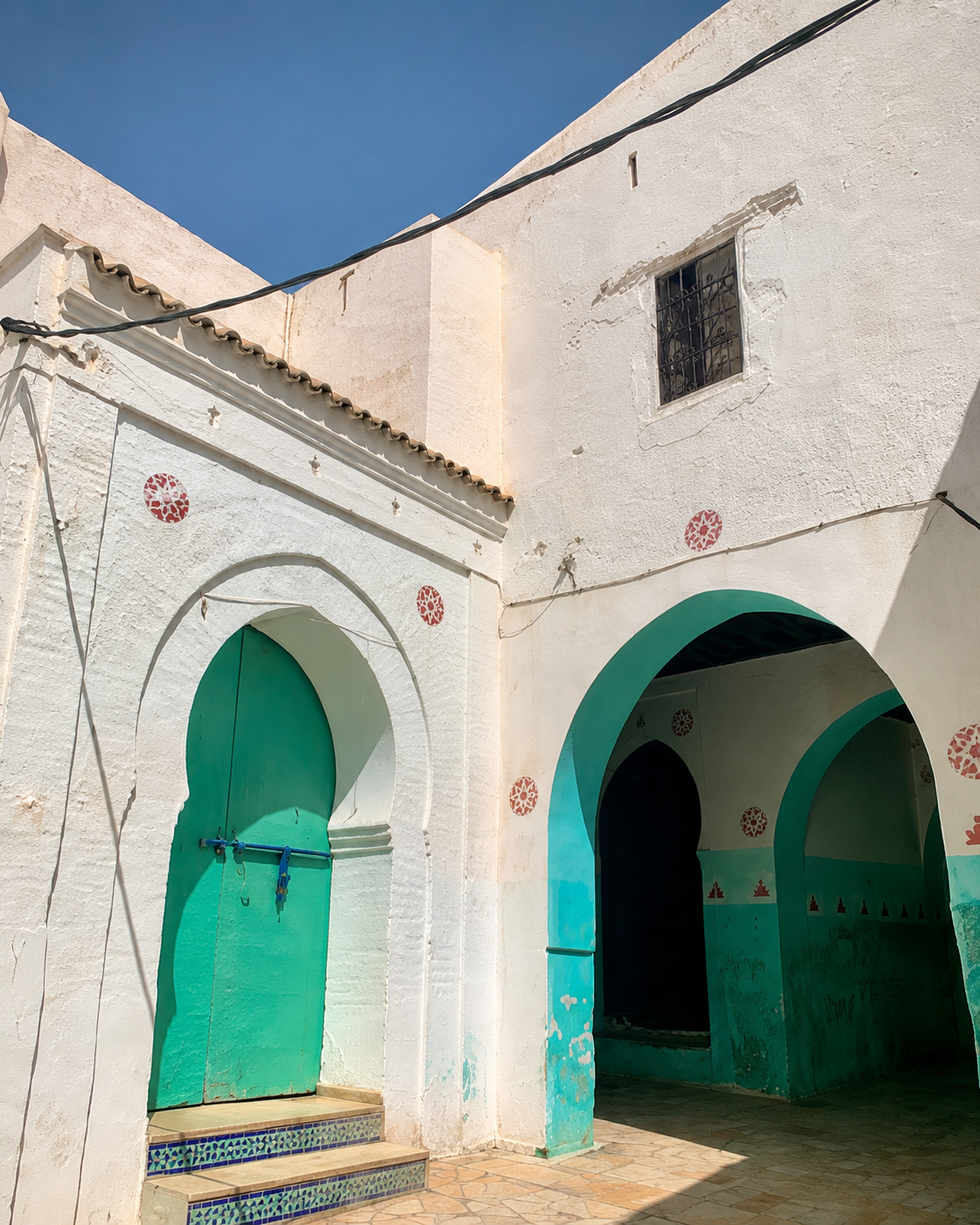 White facade with two green arched entrances and tiled thresholds