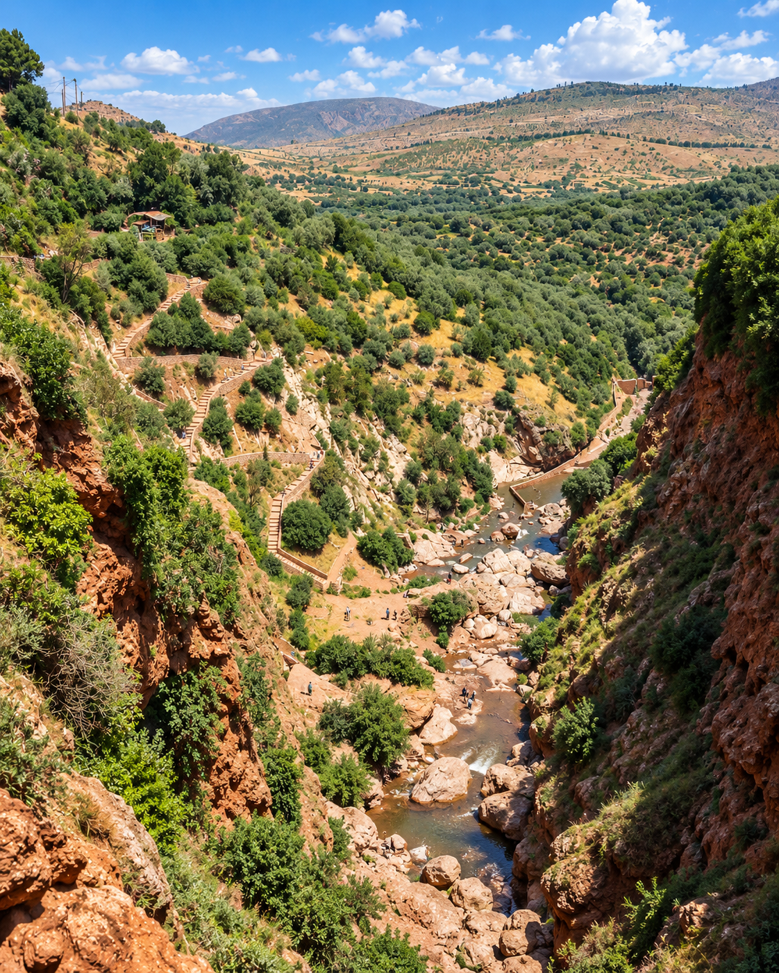 A rocky stream bed between cultivated and wooded mountain slopes