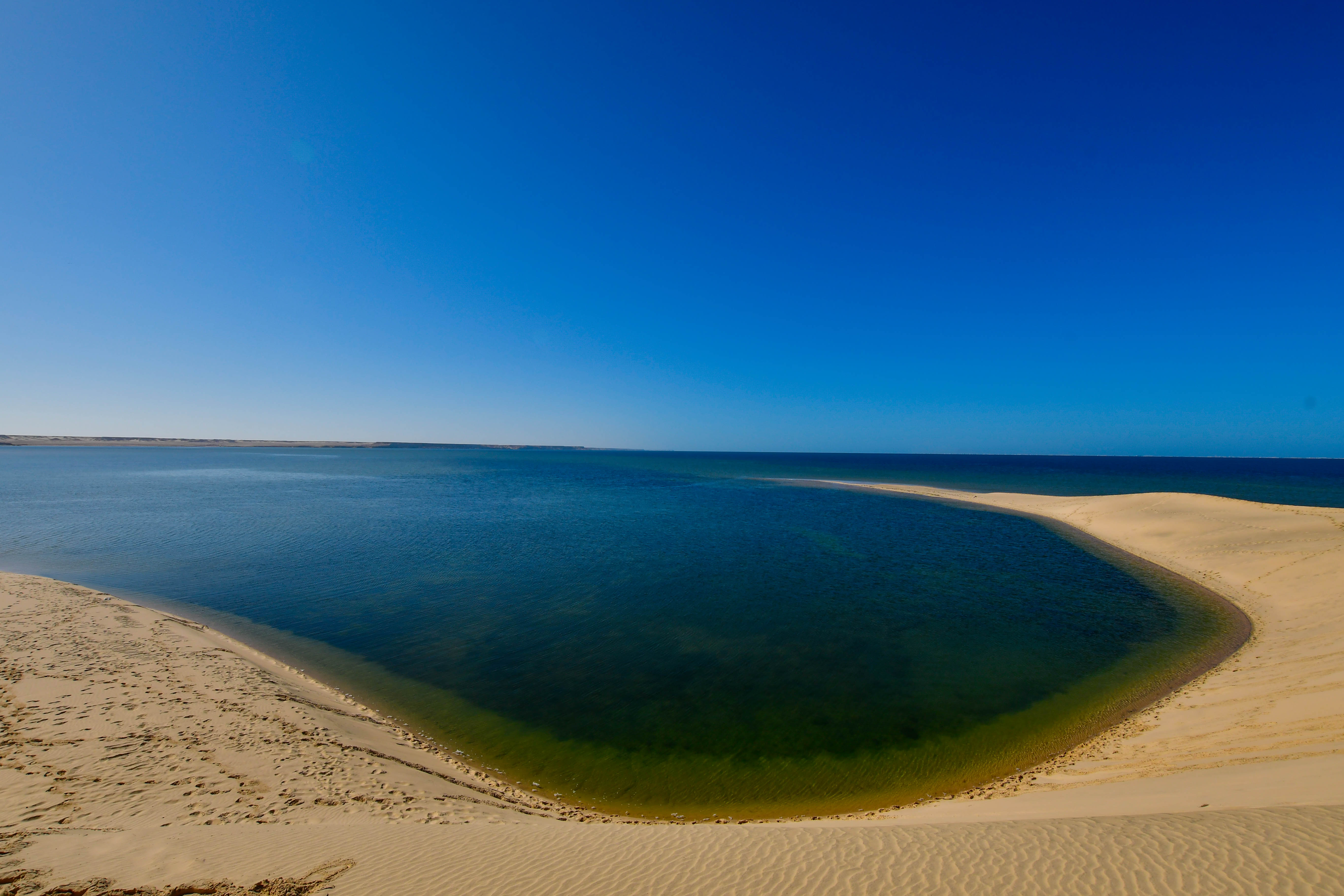 Pale sand dunes curving around the blue water of Dakhla Lagoon