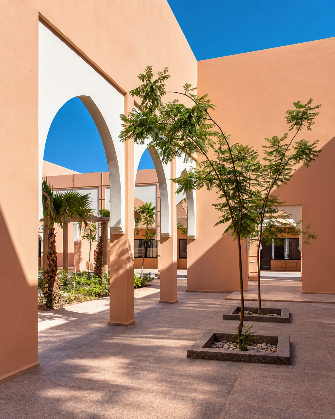 Pointed arches casting shade across a courtyard with young trees