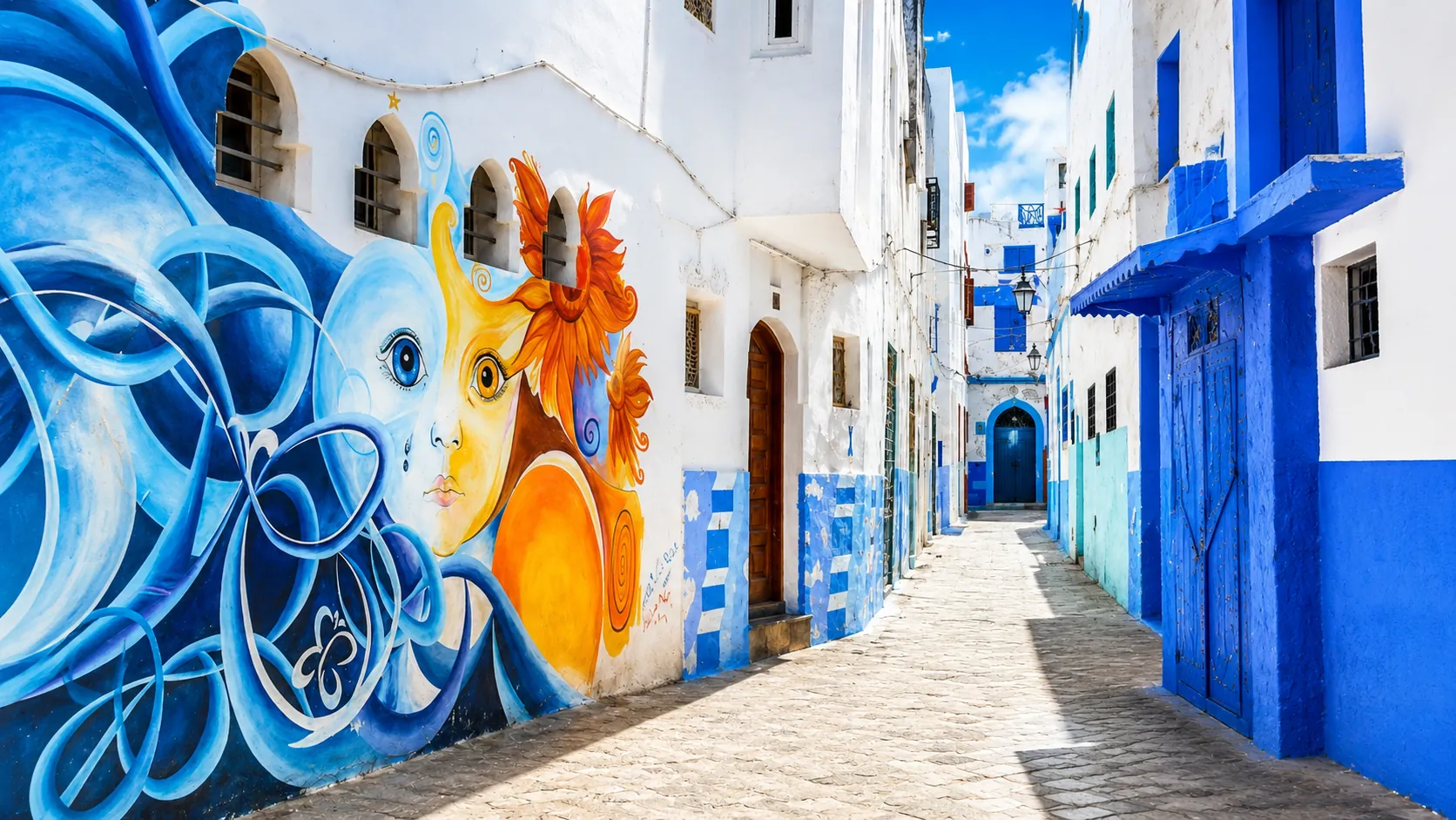 Murals and blue painted doors in a whitewashed medina lane in Asilah