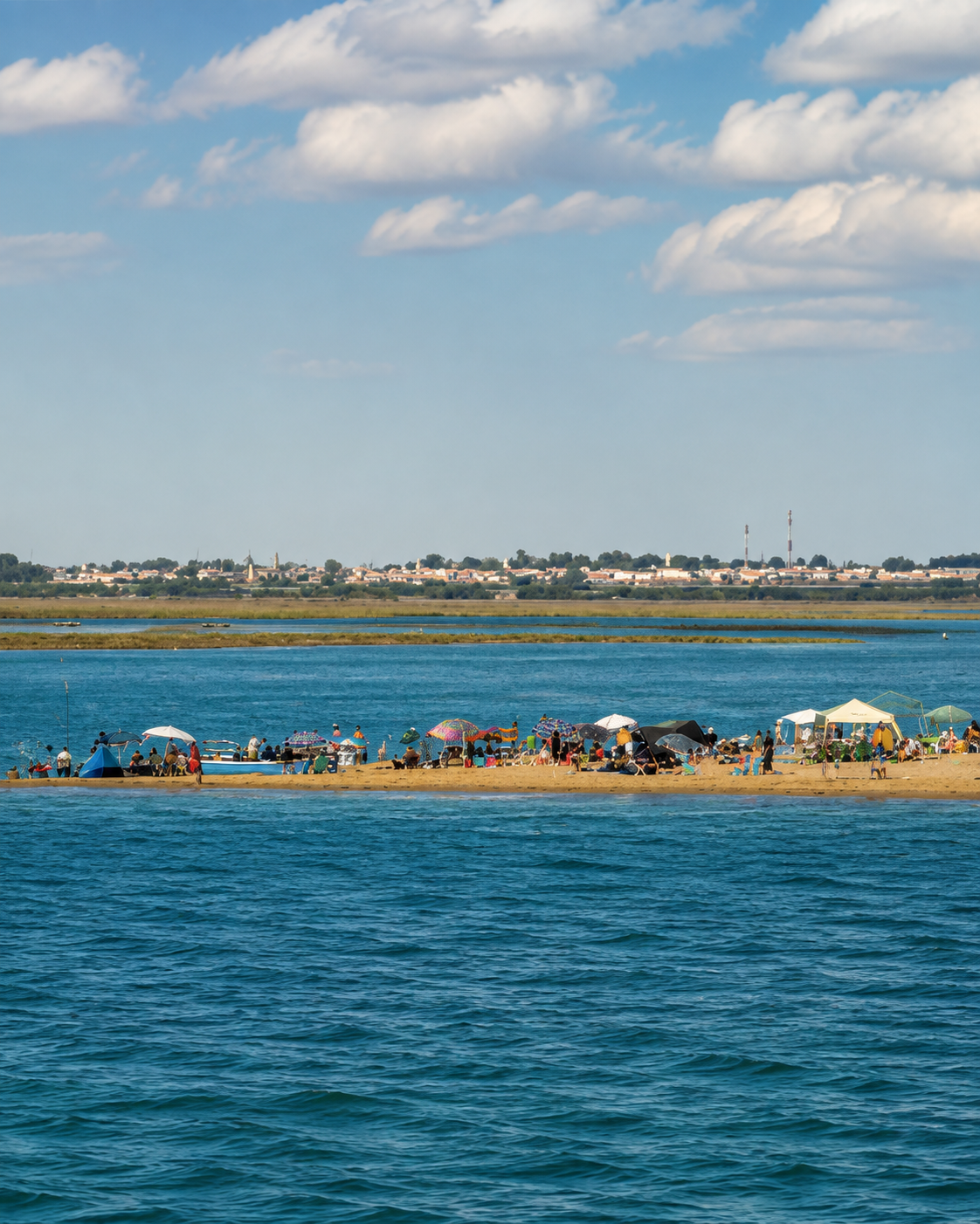 Blue lagoon water facing a low sandy shore and distant settlement