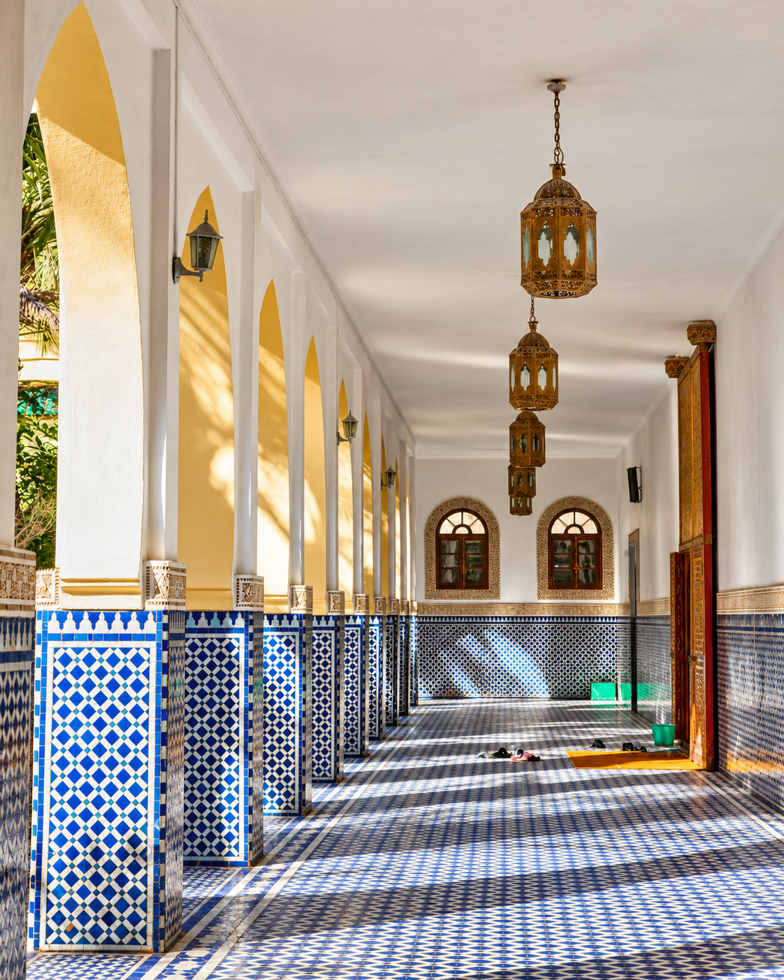 White arcades, blue-and-white zellige and hanging lanterns in a sacred interior in Rissani