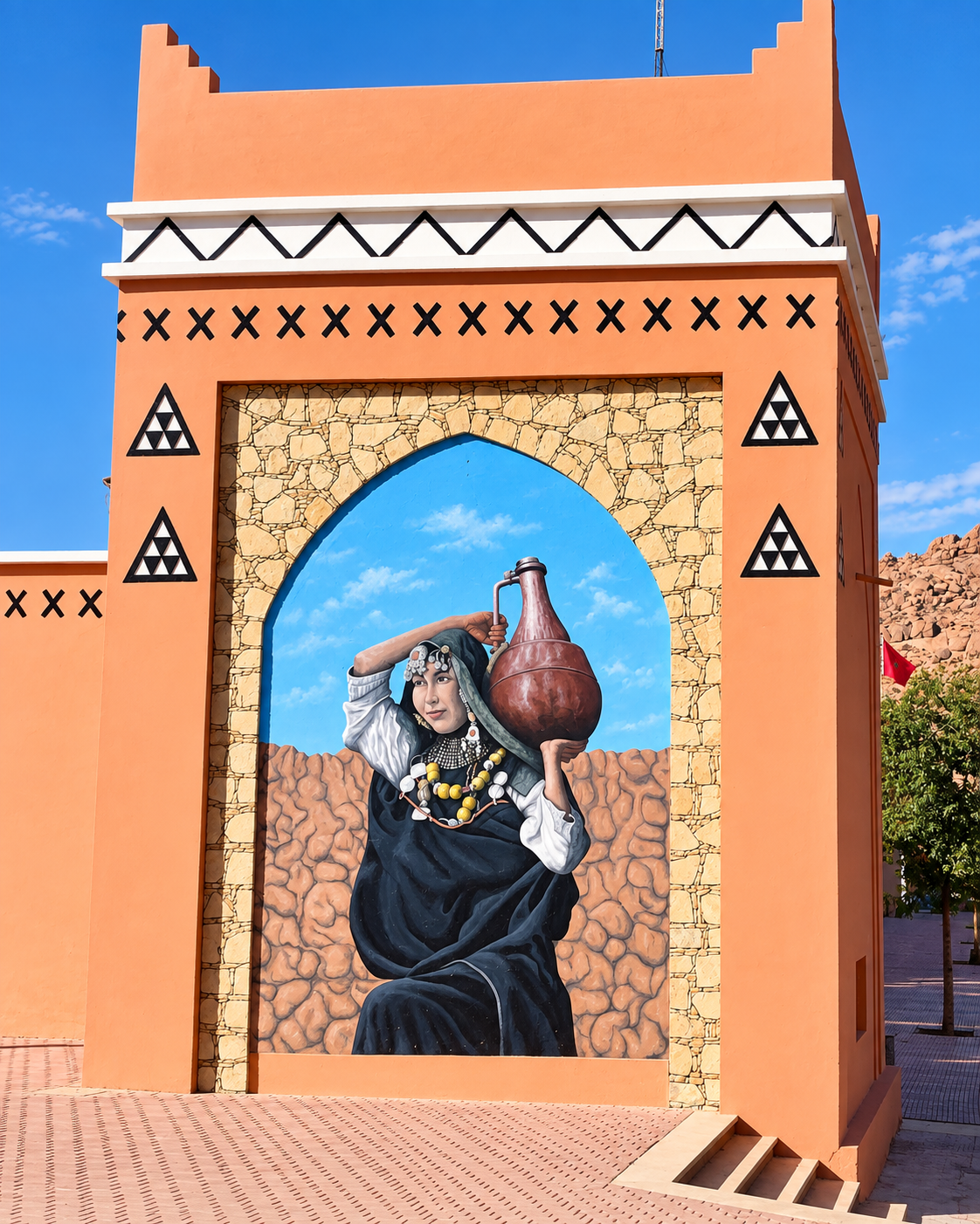 A mural of a woman in traditional dress on an ochre wall in Tafraout