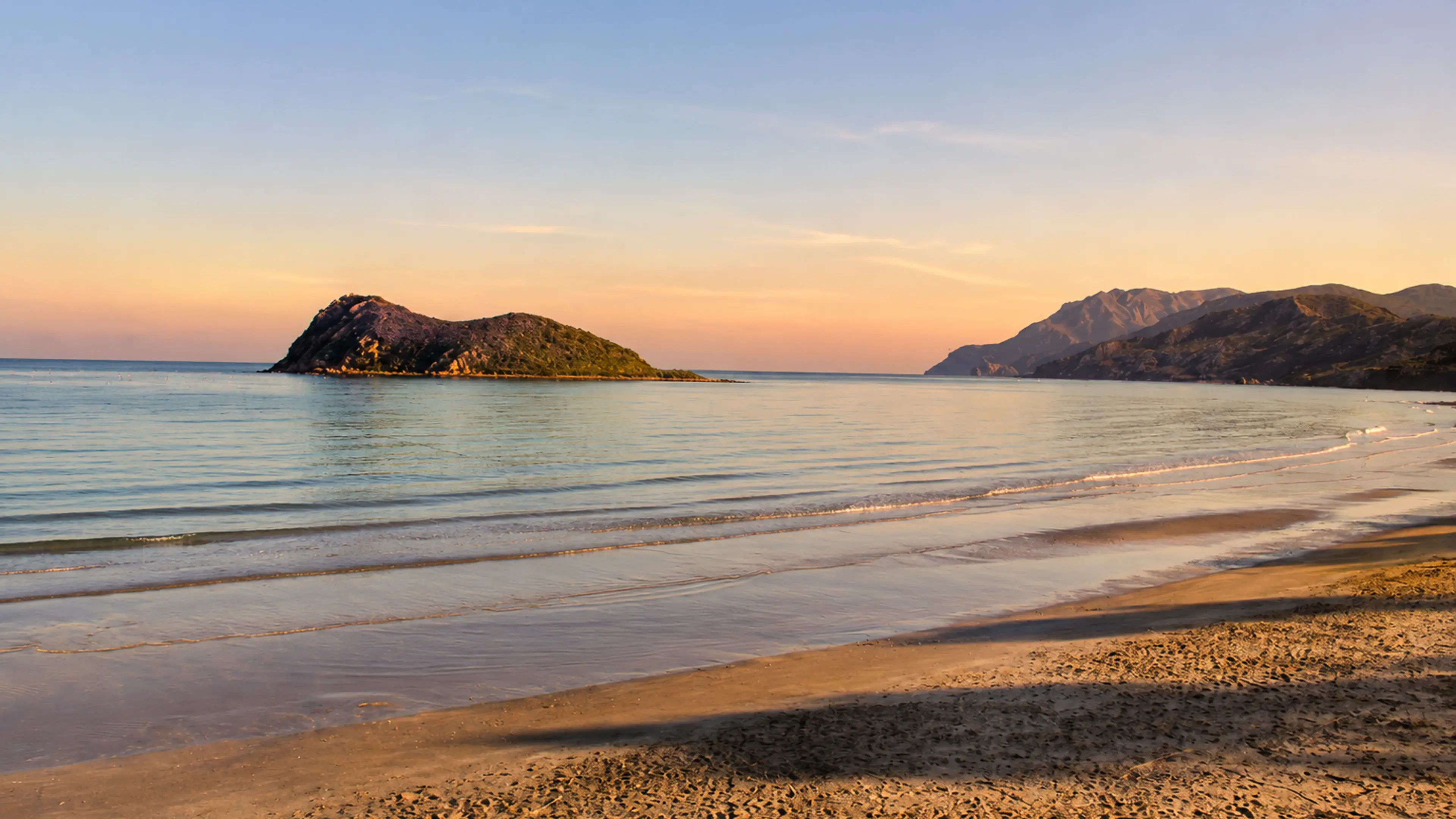 Cala Iris beach at sunset with calm Mediterranean water, an offshore islet and Rif mountains near Al Hoceima