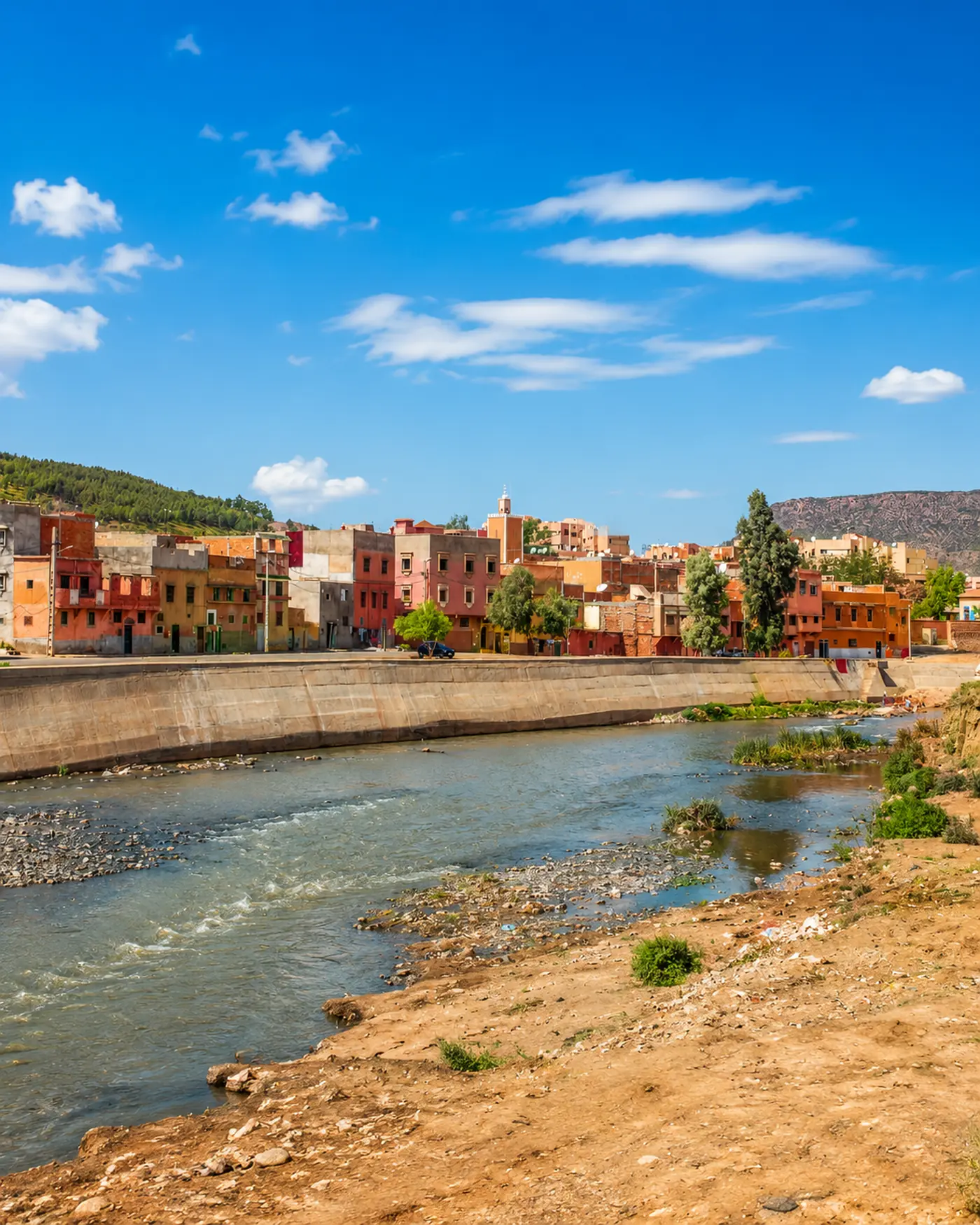 Khenifra city beside a river with colorful buildings, a mosque minaret and Middle Atlas hills under a bright sky