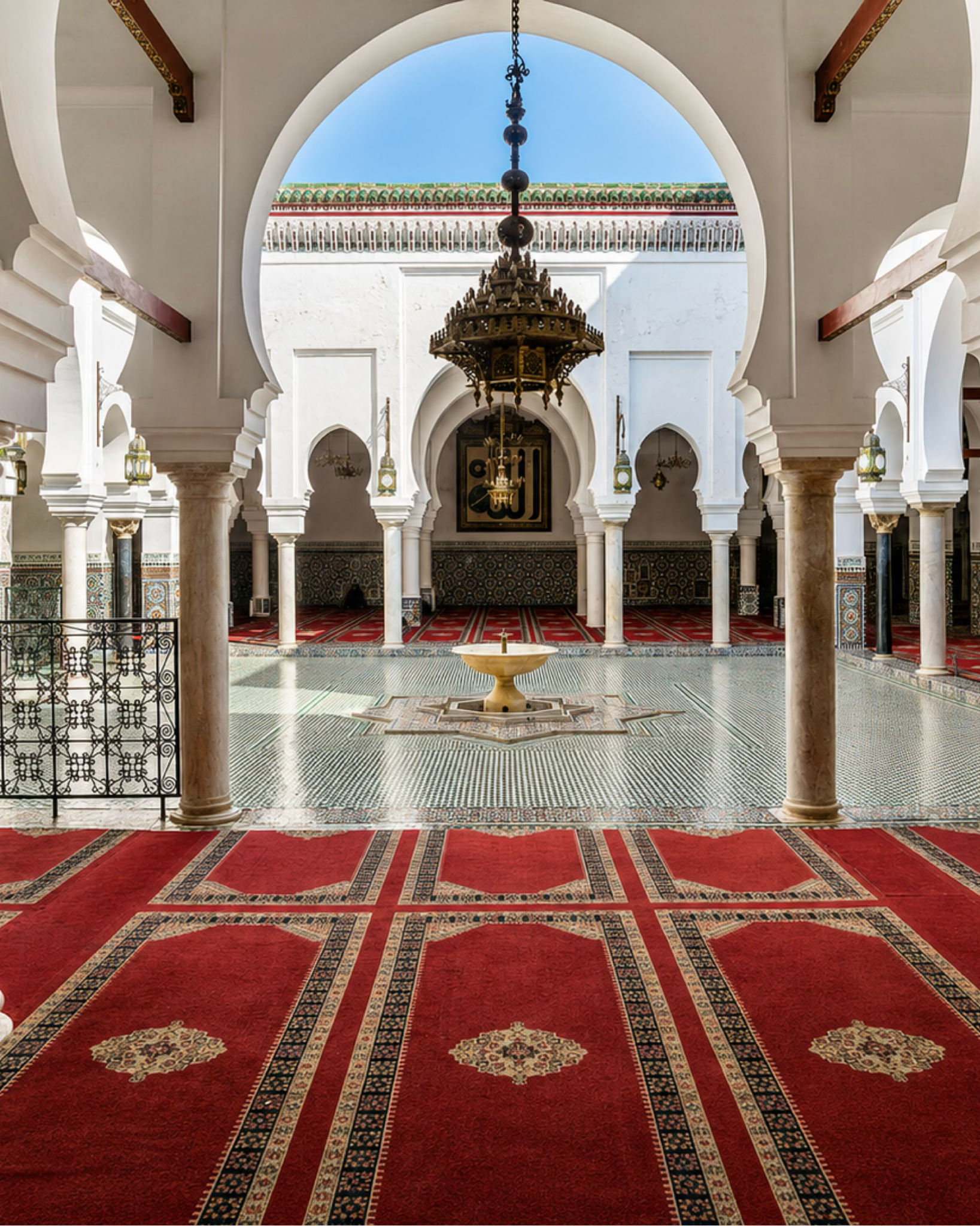 Arched interior in Fez with a courtyard fountain, zellige, carved details and hanging lamps