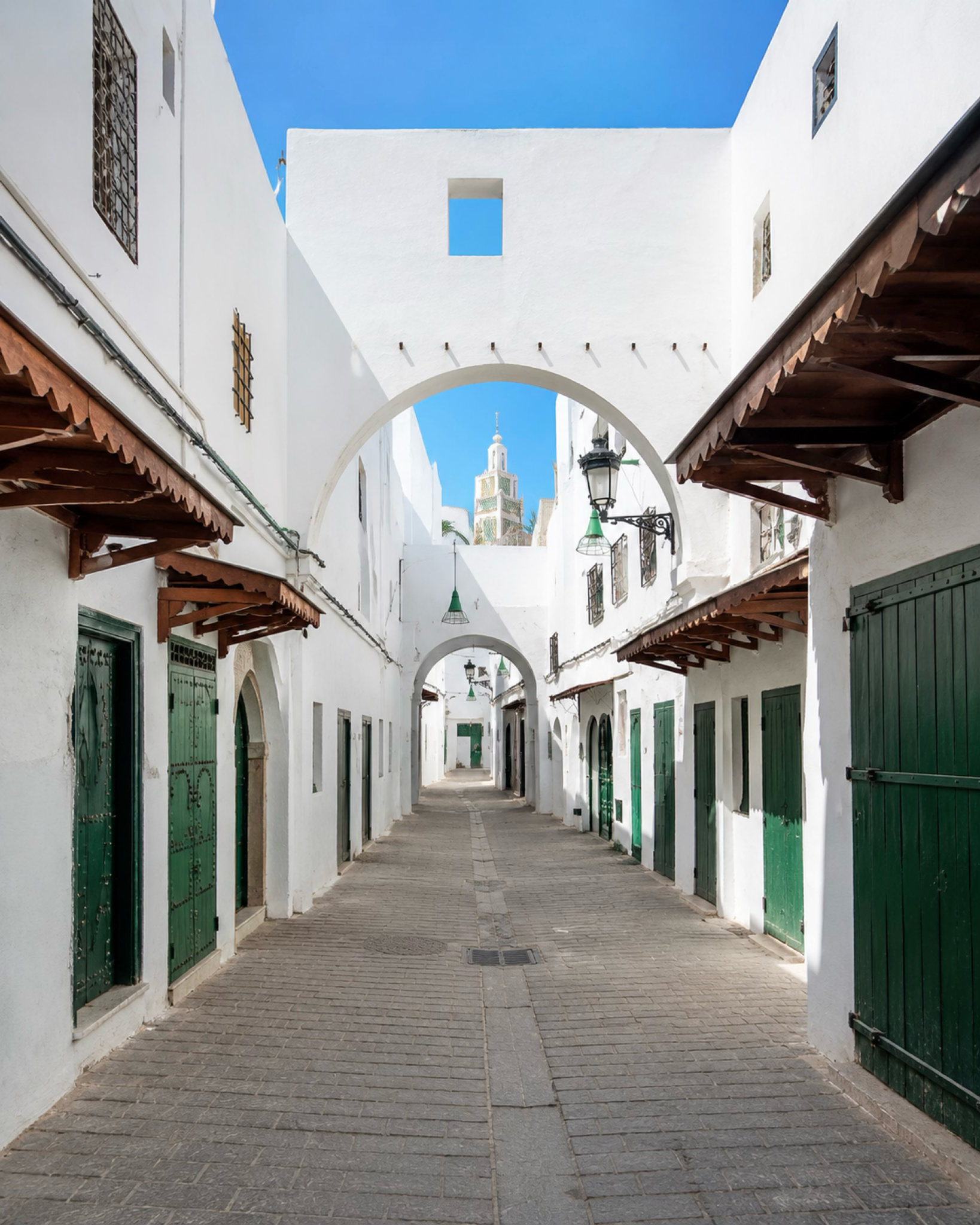 Whitewashed lane in Tétouan medina with green doors and a minaret framed by arches