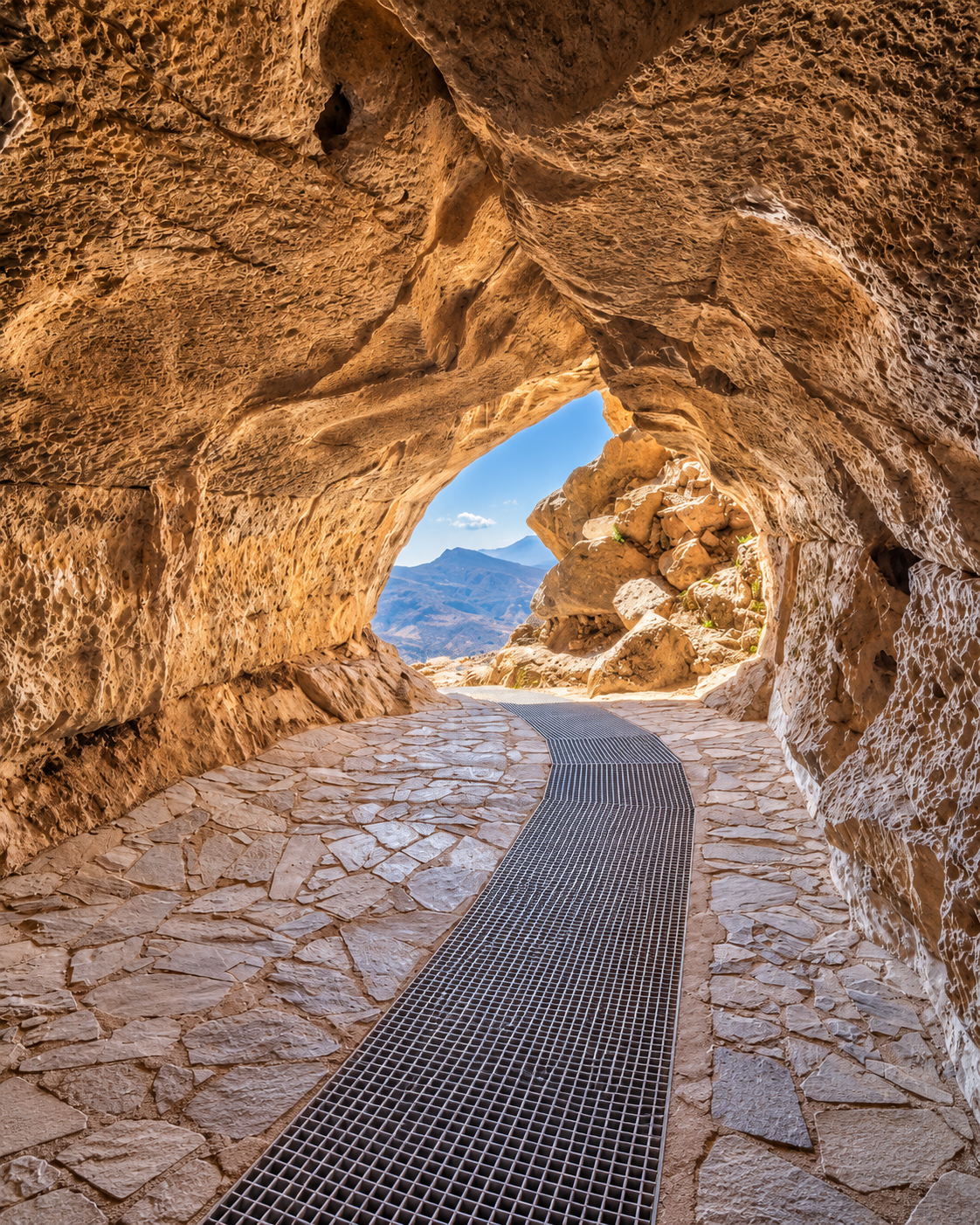 Cave opening framed by textured rock, with a path and mountain view